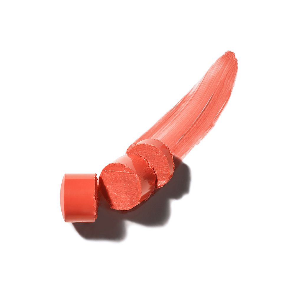 Stick di balsamo per labbra color corallo, tagliato a fette, con striscio. Su sfondo bianco.