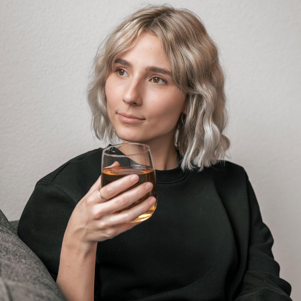 Frau hält ein Glas mit bernsteinfarbener Flüssigkeit, vermutlich Schweden Bitter.