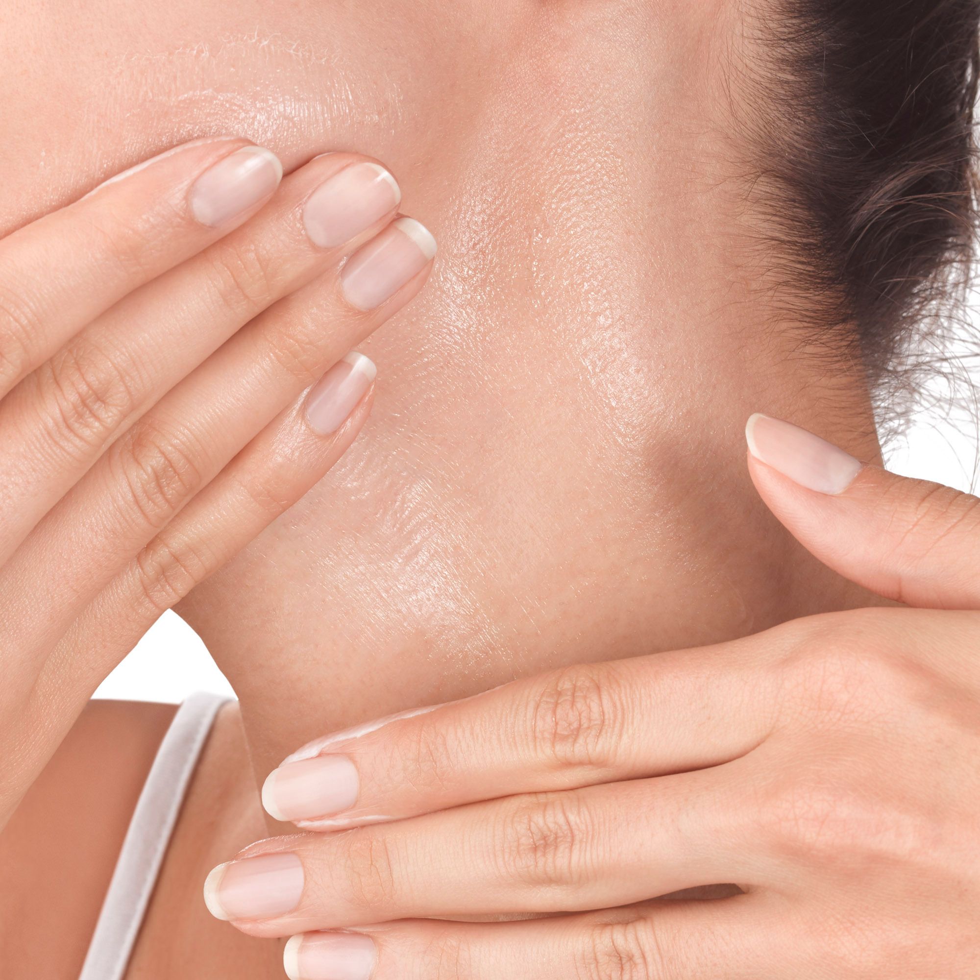 Primo piano di mani che applicano crema su collo e viso. La pelle è visibile.