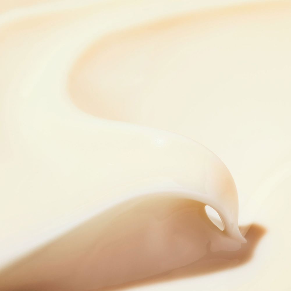 Primo piano di una crema color crema. La crema è ondulata e ha una consistenza liscia. Lo sfondo è chiaro.