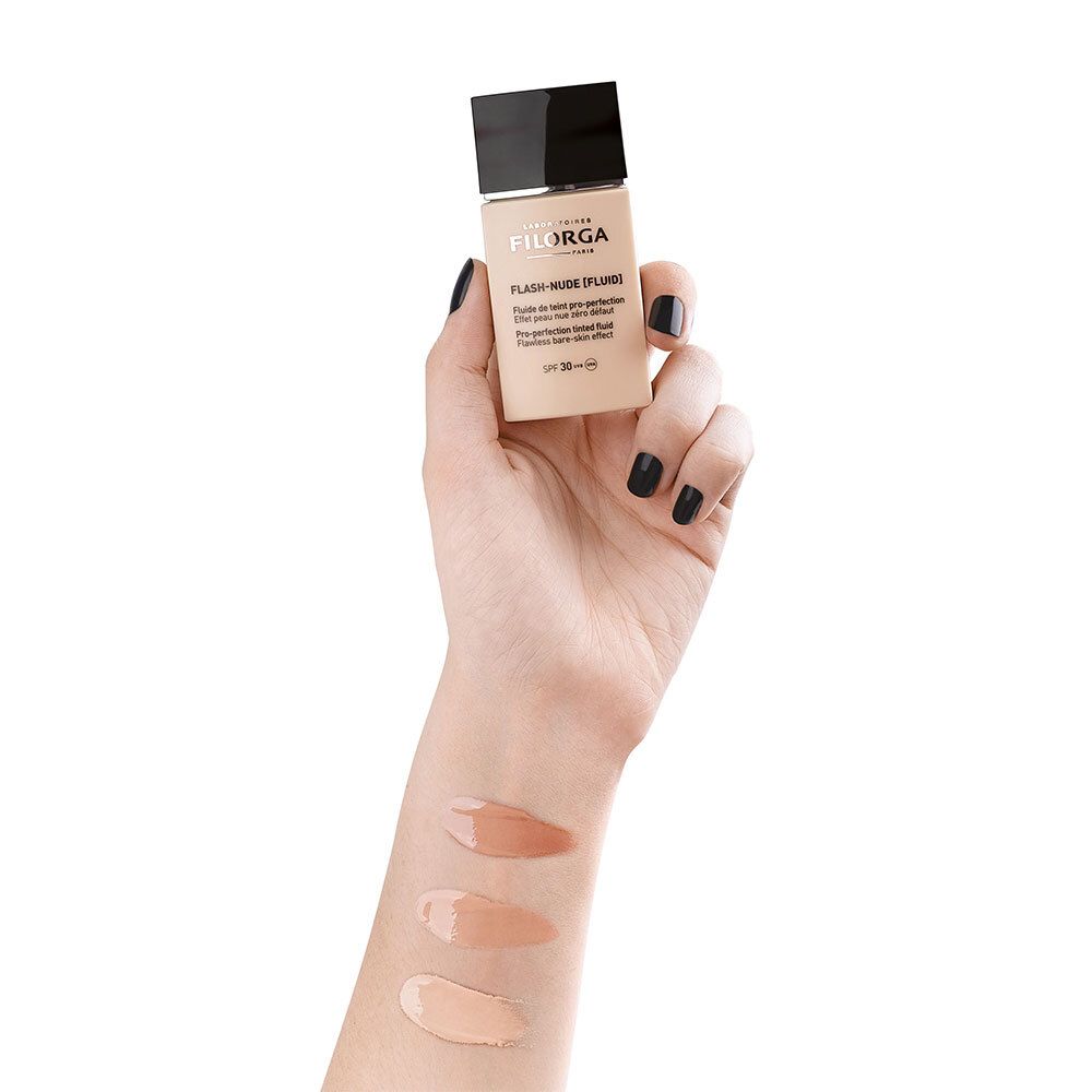 Main avec trois teintes de Filorga Flash-Nude Fluid sur le bras. Différentes nuances de beige.