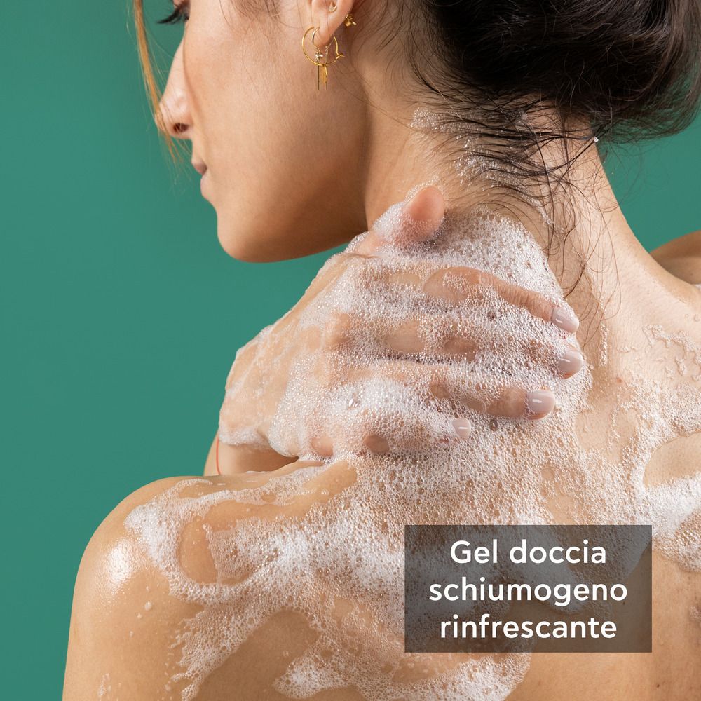 Persona si lava con schiuma. Testo: Gel doccia schiumogeno rinfrescante. Flacone: APIVITA, Refreshing Fig. Etichetta.