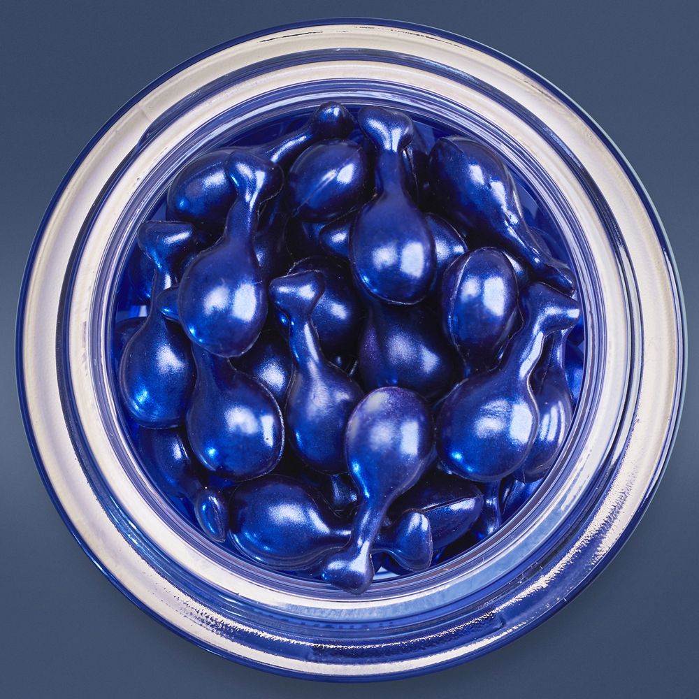 Draufsicht auf eine Dose mit blauen Perlen. Dose mit silbernem Rand. Blaue Perlen in Tropfenform.