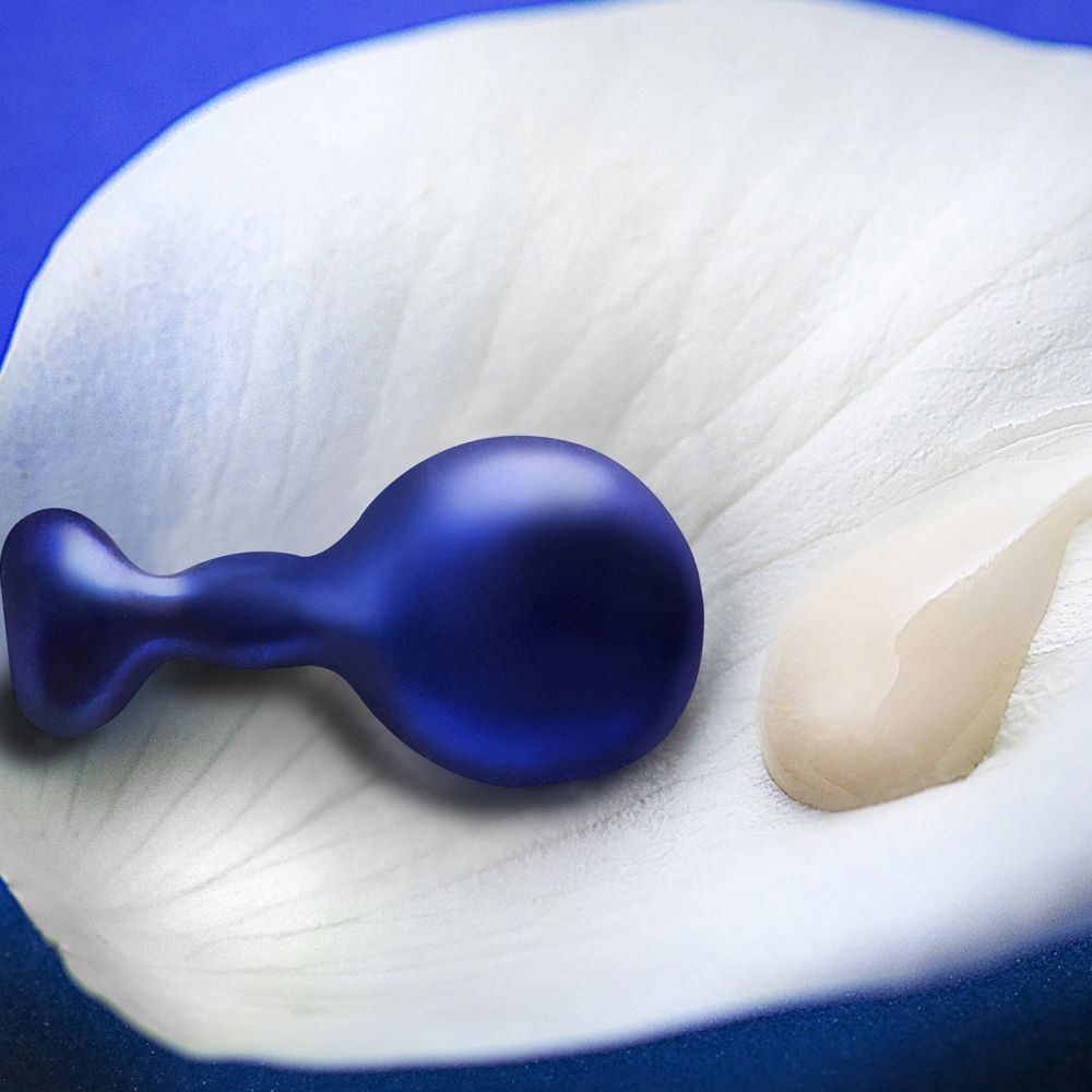 Blaue Perle und Creme auf weißem Blütenblatt. Perle in Tropfenform. Creme daneben.