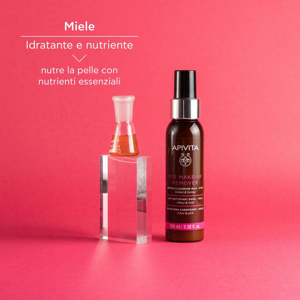 APIVITA Eye Make-up Remover accanto a contenitore di vetro. Testo: Miele, nutriente. Sfondo rosa.