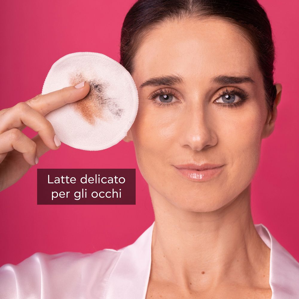 Donna si strucca con un dischetto di cotone. Testo: Latte delicato per gli occhi. Sfondo rosa.