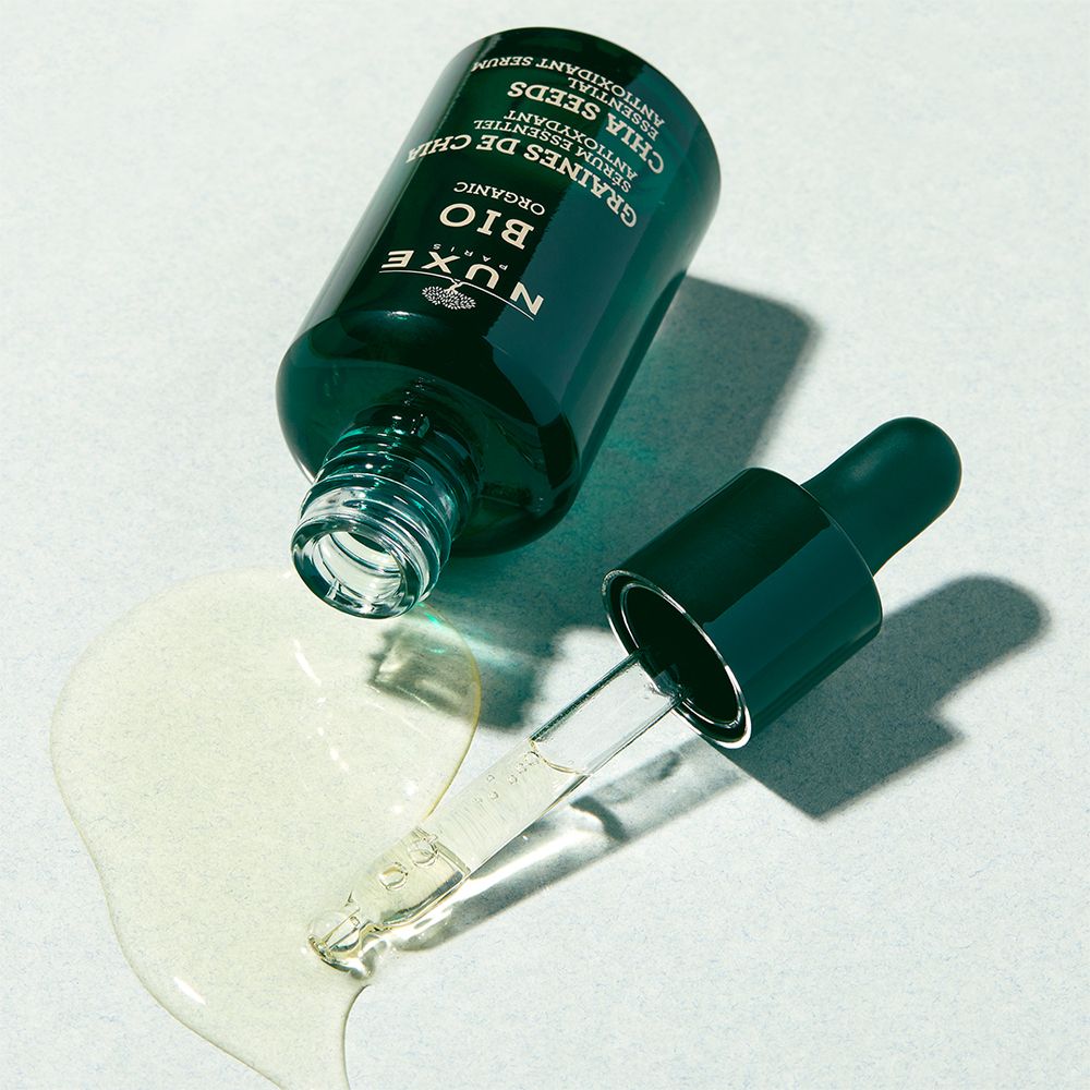Flacon en verre vert avec pipette et sérum. Sérum sur surface. Inscription : NUXE BIO, Chia Seeds.