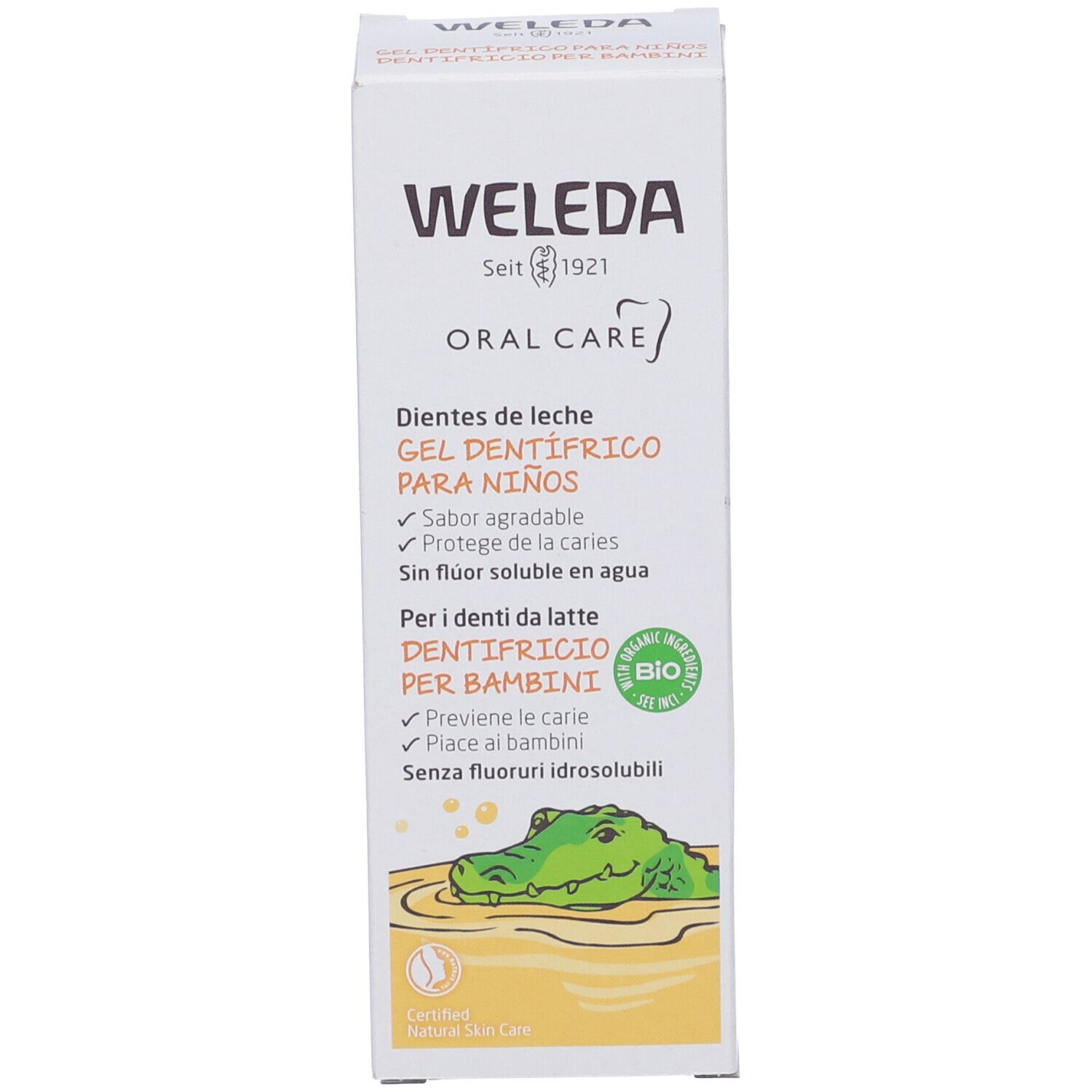 Confezione di gel dentifricio Weleda. Testo: "Oral Care", "Gel dentifrico para niños". Certificazione bio. Illustrazione di un coccodrillo. Orientamento verticale.