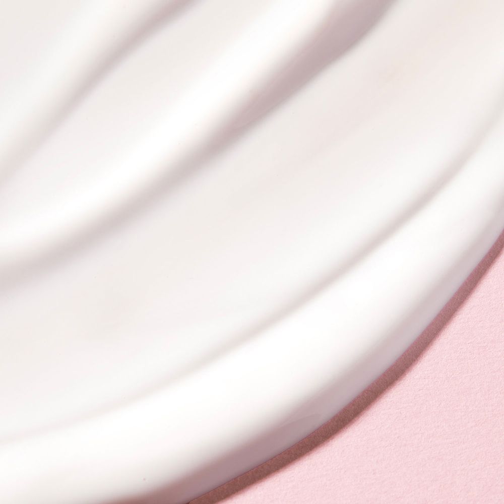 Gros plan sur une crème blanche sur fond rose. Texture ondulée. Aucune inscription visible.