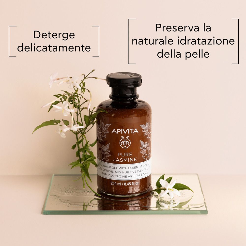 Braune Flasche mit schwarzem Deckel auf Glasplatte. Aufschrift: APIVITA Pure Jasmine Duschgel. Weiße Jasminblüten.
