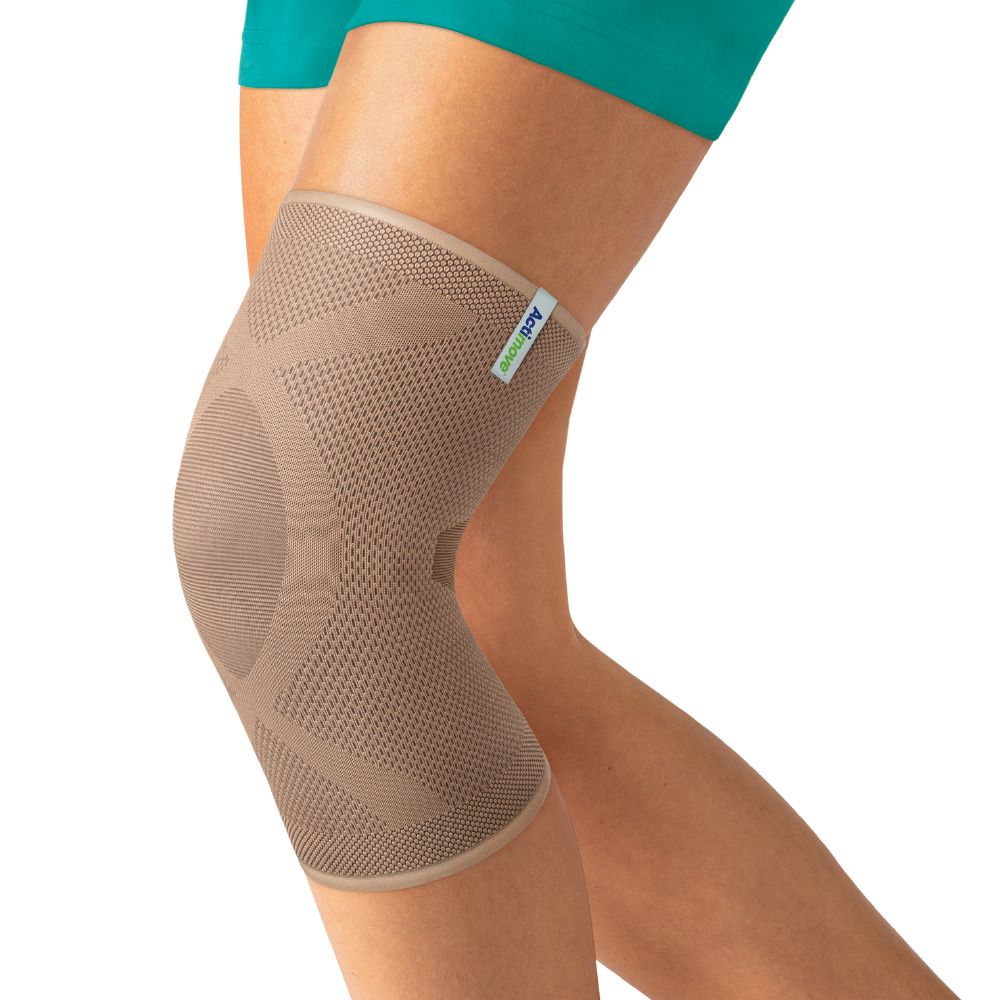 Person trägt beige Actimove Kniebandage. Geschlossene Patella. Auf hellem Hintergrund.