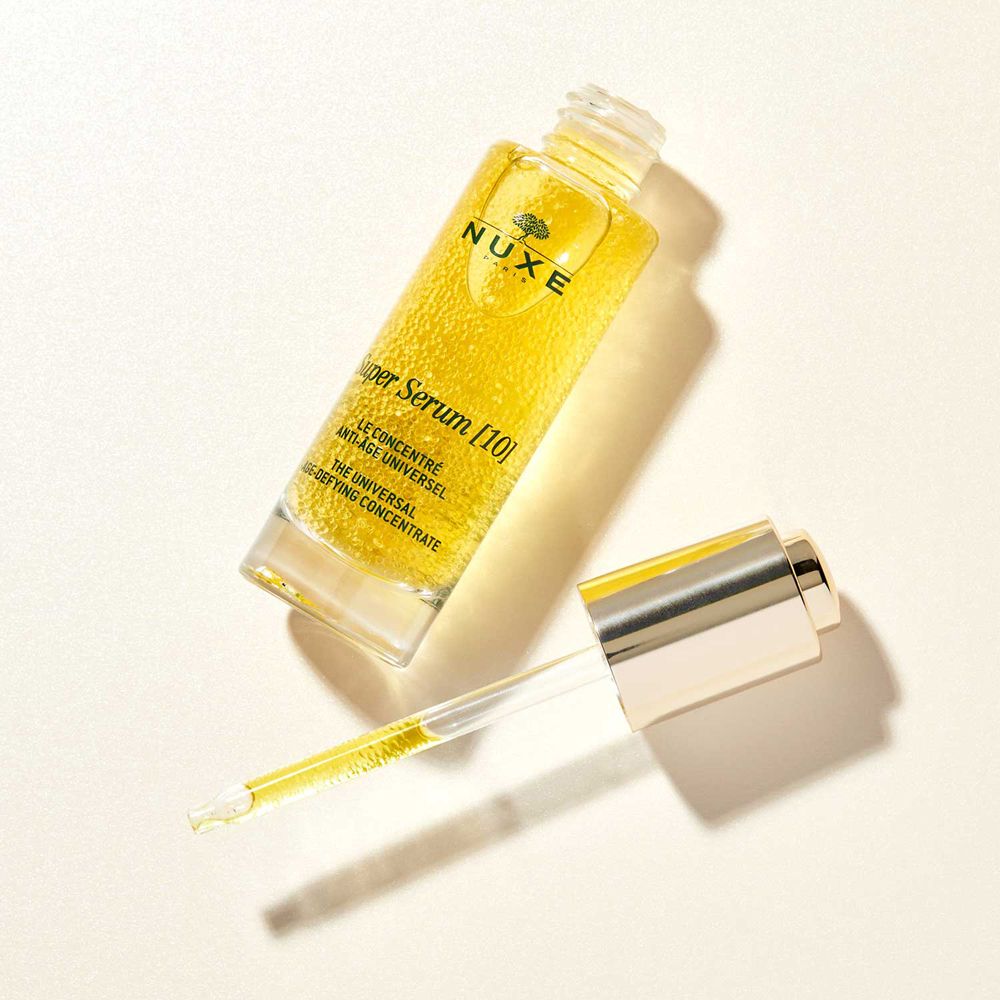 Flacone di siero dorato e pipetta. Scritta: NUXE Super Serum [10].