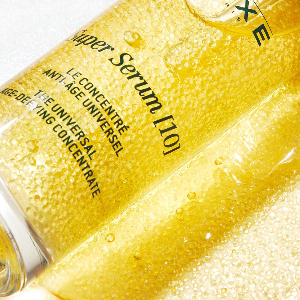 Primo piano di siero dorato. Scritta: NUXE Super Serum [10].