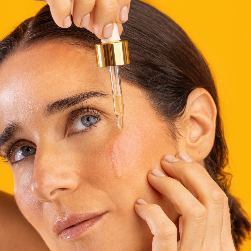 Donna che applica olio sulla pelle con un contagocce. Sfondo giallo. Cura della pelle.