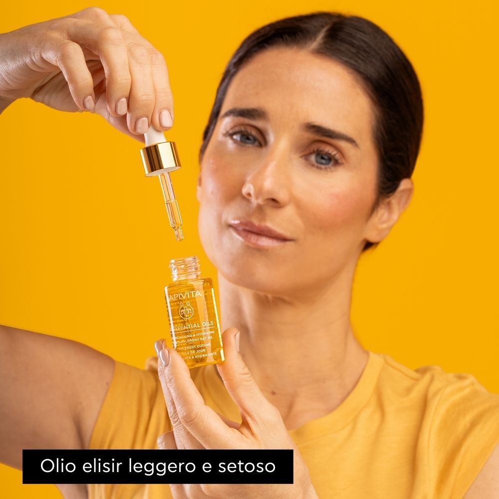 Donna che tiene un flacone di olio con un contagocce. Sfondo giallo. Testo: Olio elisir leggero e setoso.