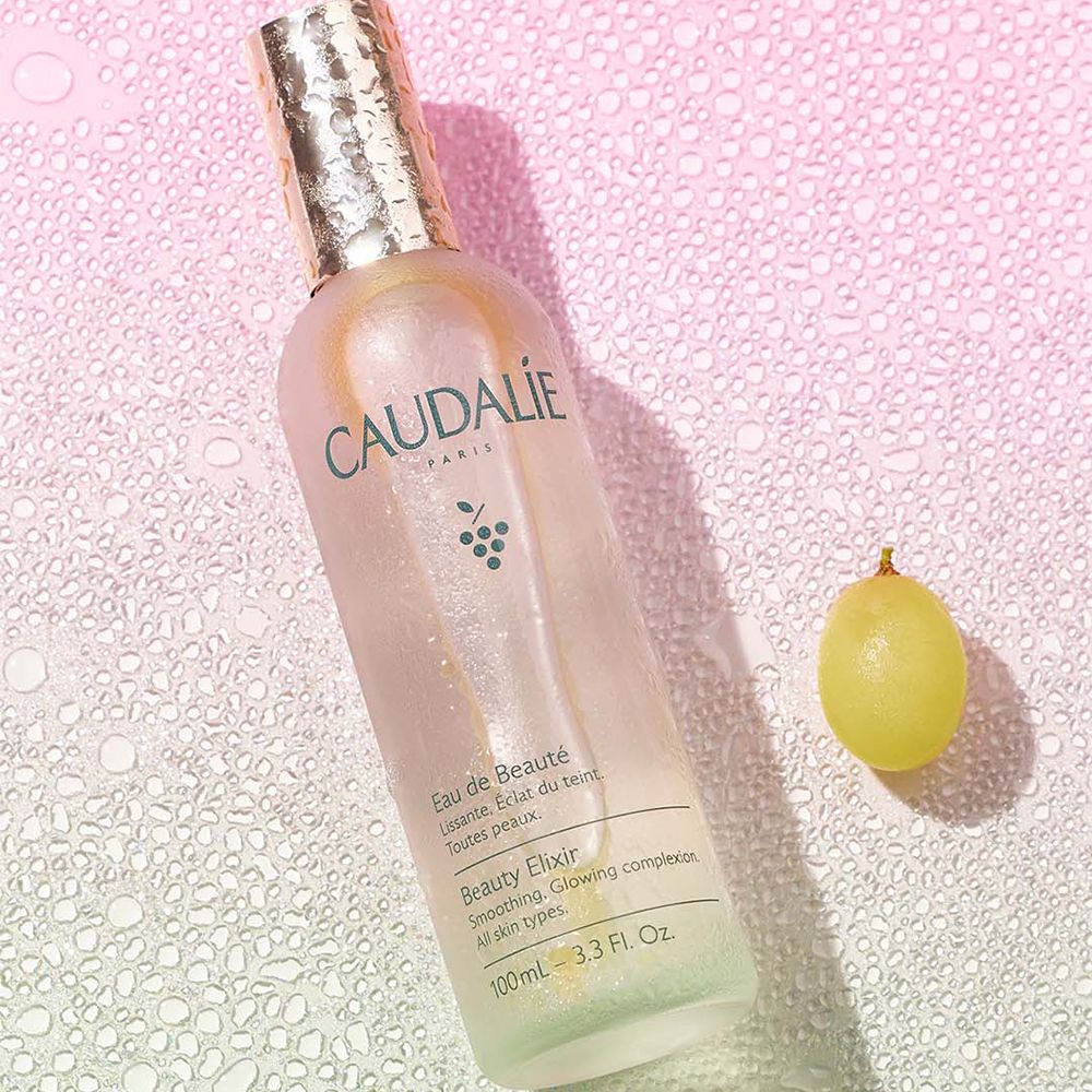 Flacone Caudalie Eau de Beauté, tappo argentato con gocce d'acqua. Sfumatura rosa-verde, testo Caudalie.