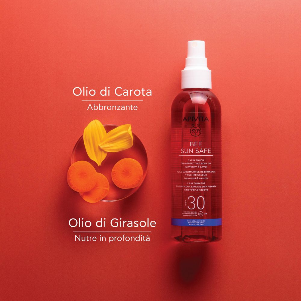 Olio APIVITA Bee Sun Safe e ingredienti. Olio di carota e girasole. Sfondo rosso.