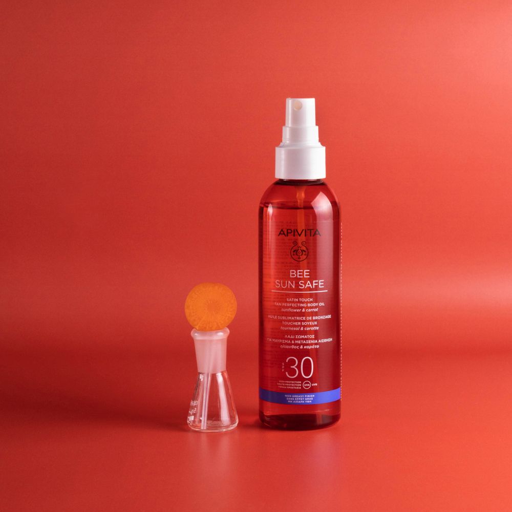 Olio APIVITA Bee Sun Safe e accessori. Liquido rosso. SPF 30. Contenitore di vetro con contenuto arancione.