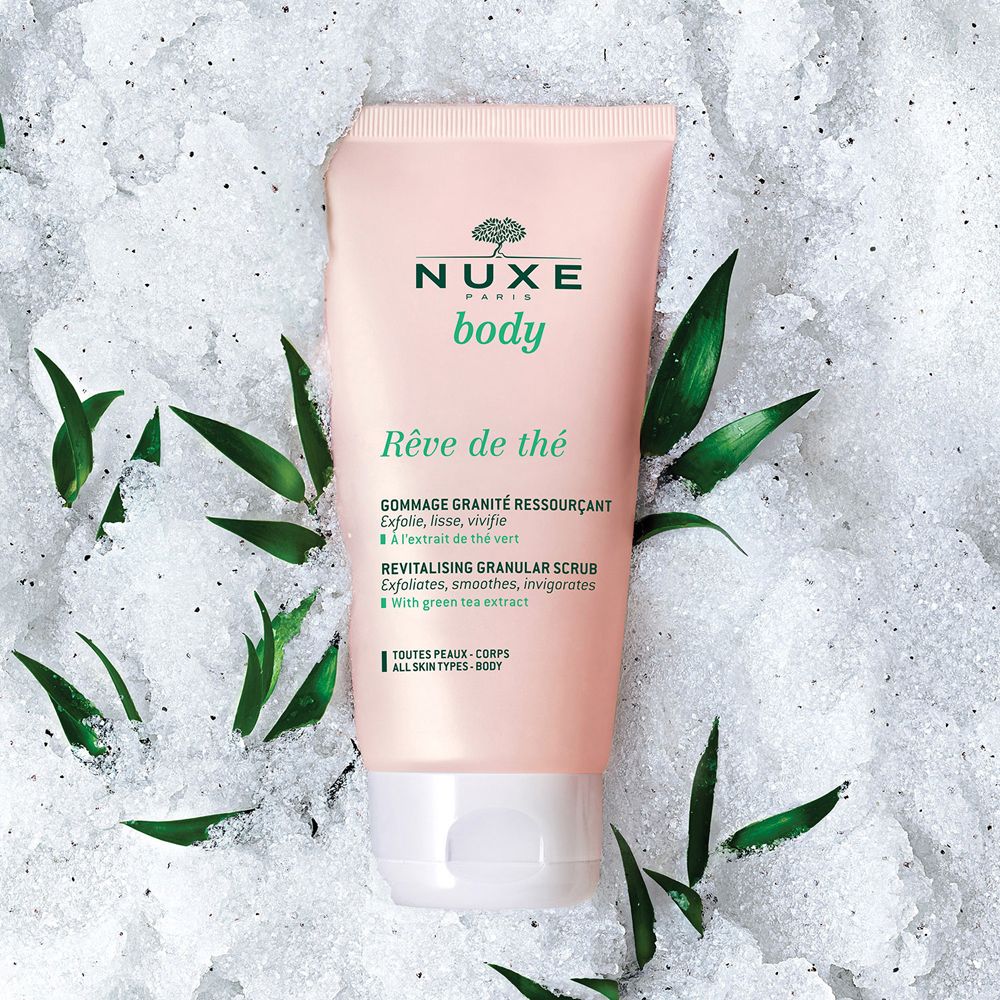 Tubo rosa con tappo bianco, su sfondo bianco con foglie. Scritta: Nuxe Body, Rêve de Thé, Revitalising Granular Scrub.
