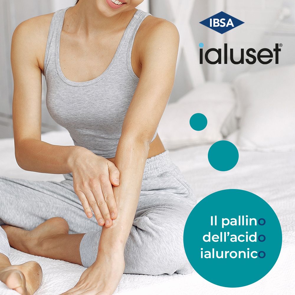Donna con canotta e pantaloni grigi. Applica la crema sul braccio. Logo Ialuset in alto a destra.