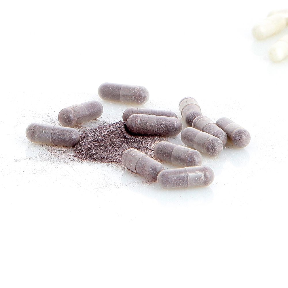 Grijze capsules en poeder op witte achtergrond. Geen verpakking zichtbaar.