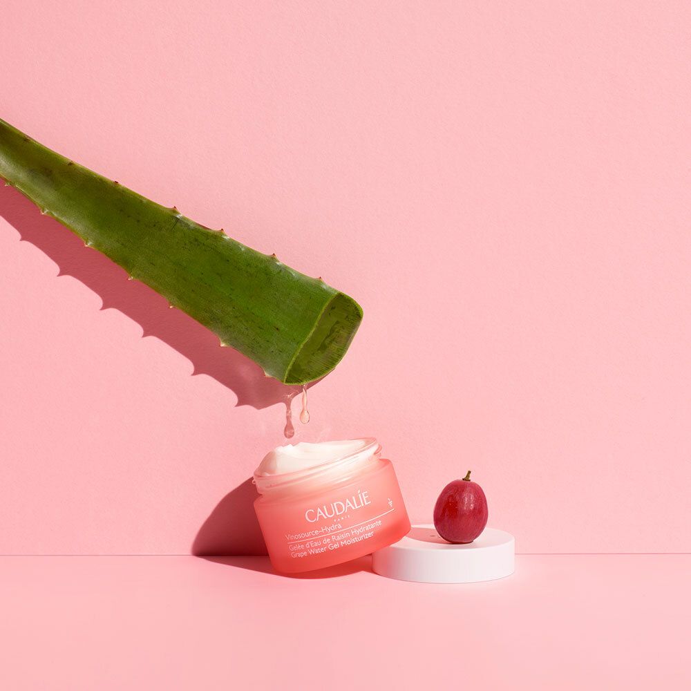 Vaso rosa con foglia di aloe vera e uva. Scritta: CAUDALIE, Vinosource-Hydra, Gelée d'Eau de Raisin Hydratante, Grape Water Gel Moisturizer.