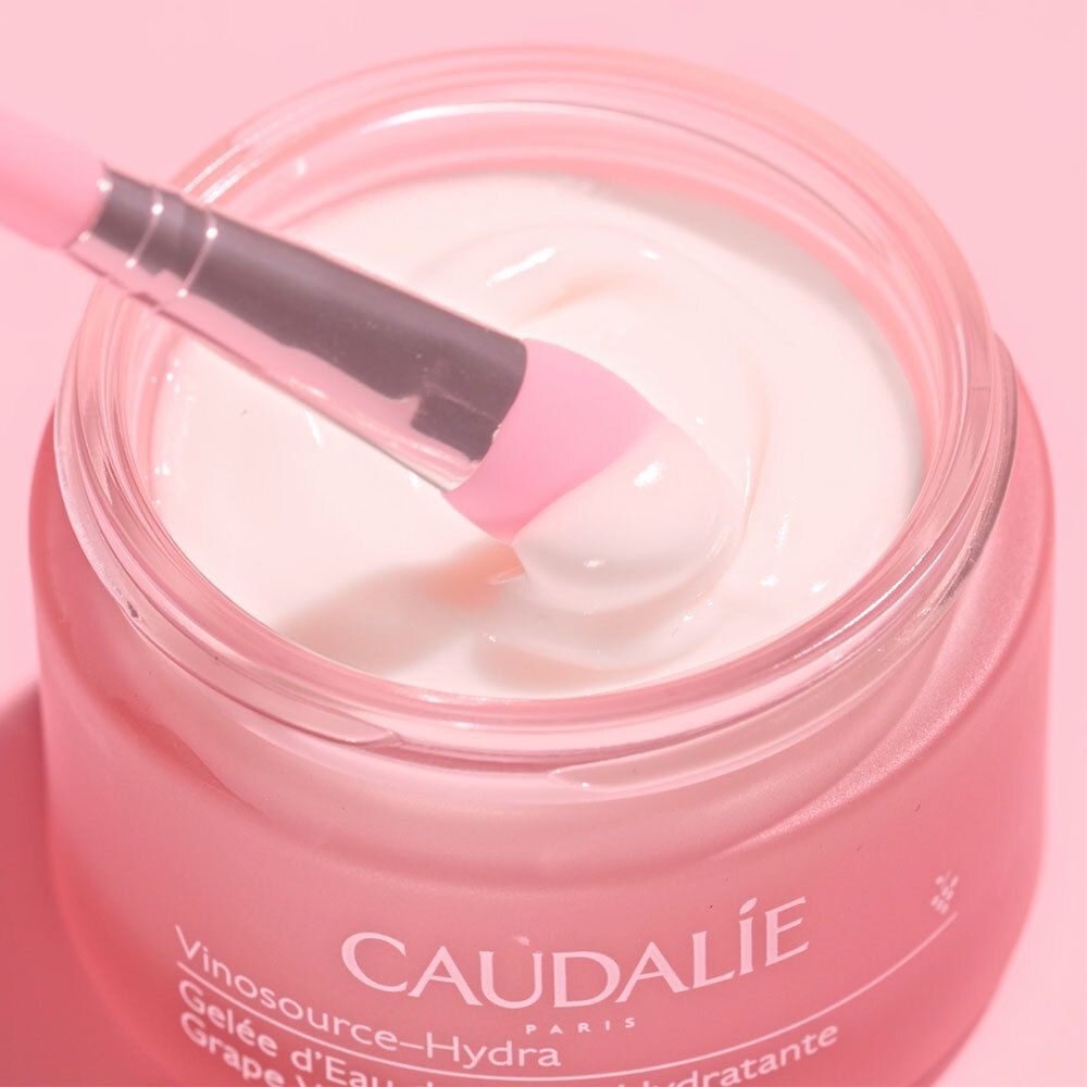 Vaso rosa con pennello. Scritta: CAUDALIE, Vinosource-Hydra, Gelée d'Eau de Raisin Hydratante, Grape Water Gel Moisturizer.