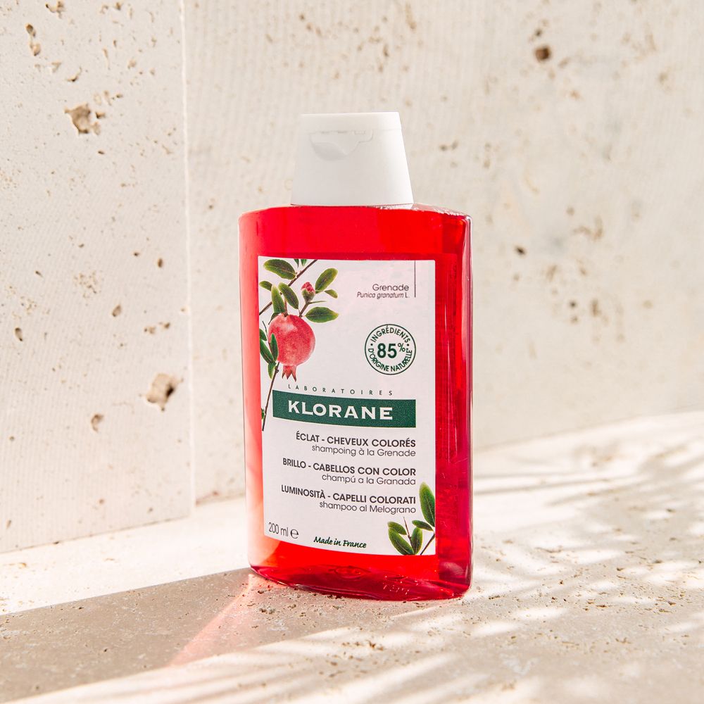 Rote Shampoo-Flasche mit weißem Deckel. Aufschrift: Klorane, Éclat Cheveux Colorés, 85% natürliche Inhaltsstoffe. Auf hellem Hintergrund.