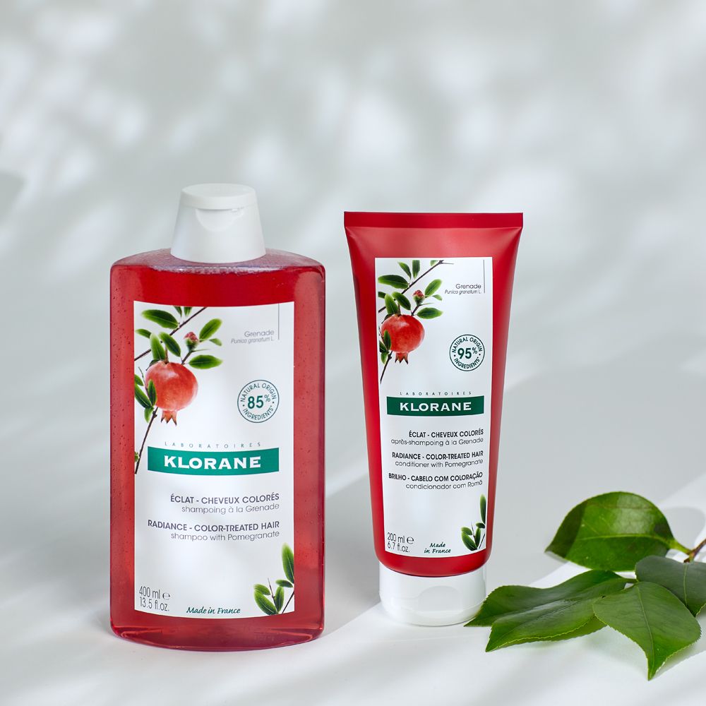 Due prodotti: flacone e tubo di shampoo rossi. Entrambi con etichetta KLORANE e illustrazione di melograno.