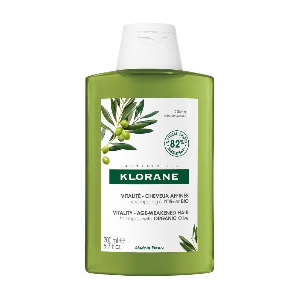 Flacon de shampooing vert avec bouchon blanc. Inscription: KLORANE, Vitalité - Cheveux Affinés, Shampooing à l'Olivier Bio. Illustration d'olives.