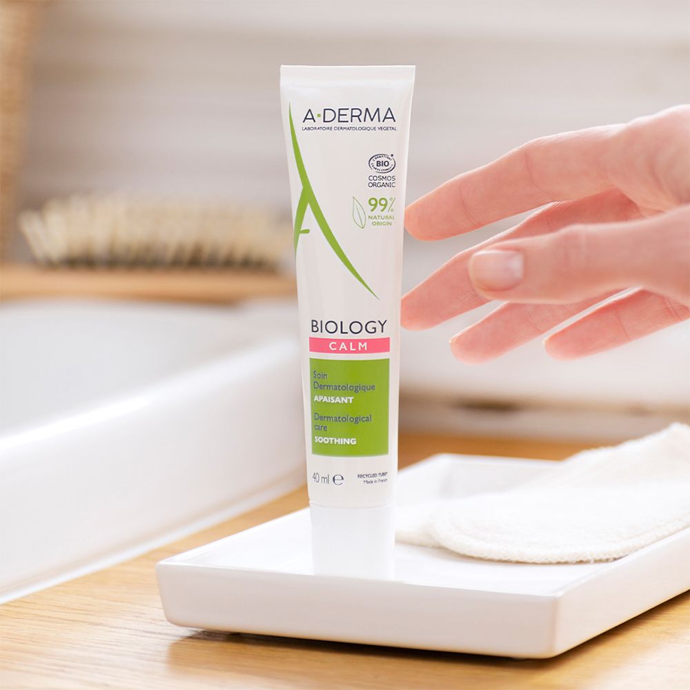 Mano che tiene un tubo di crema. Dischetti di cotone su un vassoio bianco. Sfondo bagno.
