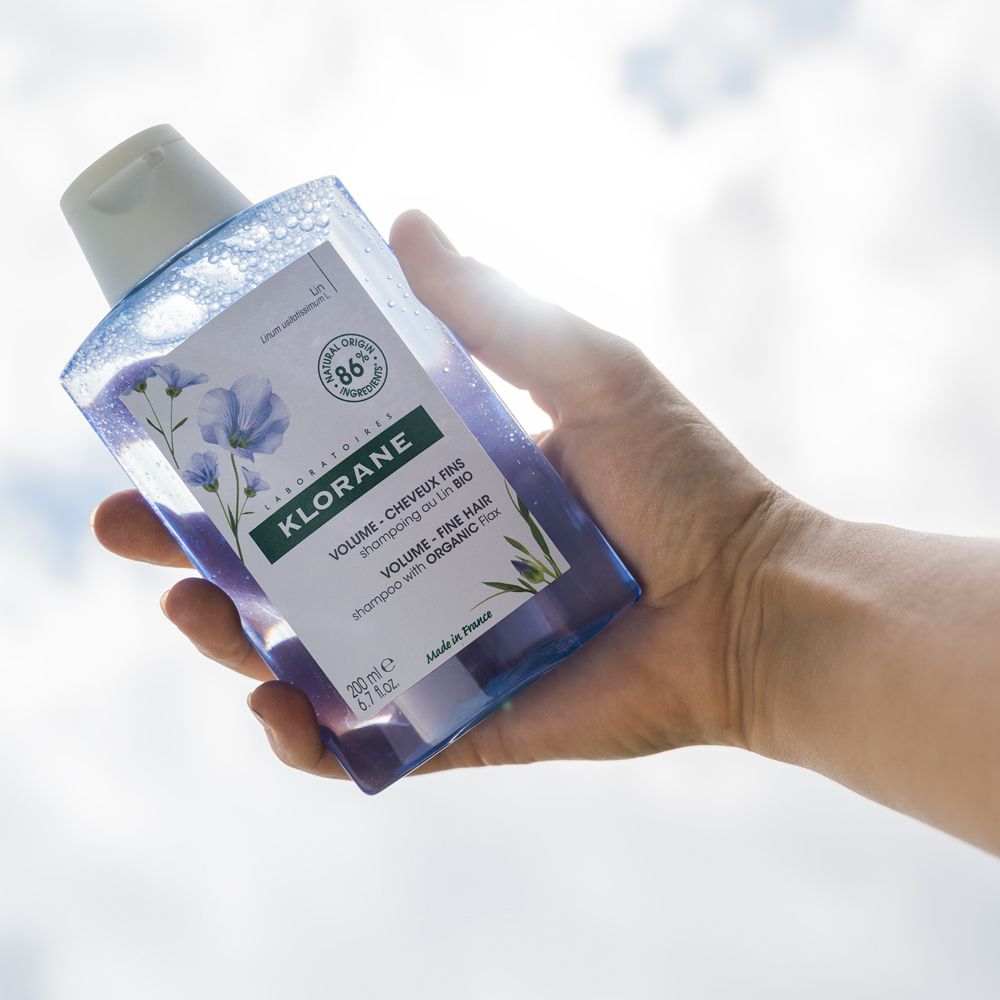 Mano che tiene un flacone di shampoo blu. Lo sfondo è un cielo soleggiato.