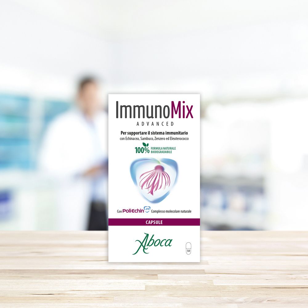 Produktverpackung auf einem Tisch. Text: Immunomix Advanced, Aboca, 100% biologisch abbaubar. Hintergrund: verschwommene Person.