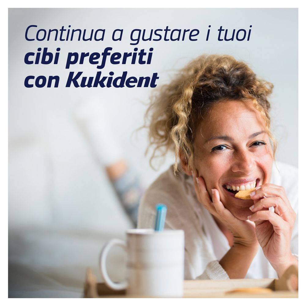Donna sorridente mangia biscotto. Tazza, vassoio. Testo: Continua a gustare i tuoi cibi preferiti con Kukident.