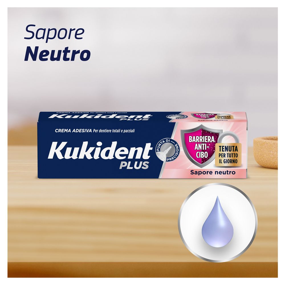 Produktverpackung auf Holz. Aufschrift: Kukident Plus, Barriera Anti-cibo, Tenuta per tutto il giorno.