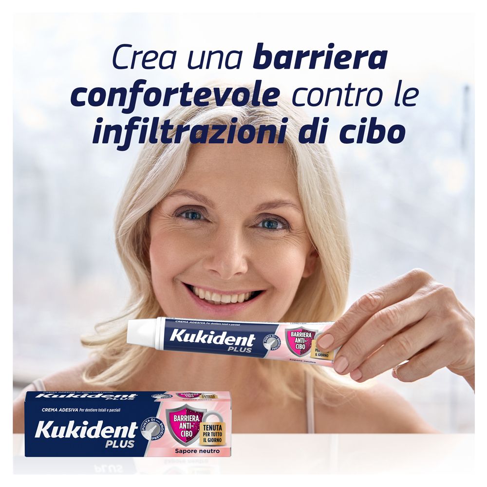 Frau hält Tube. Aufschrift: Kukident Plus, Barriera Anti-cibo, Tenuta per tutto il giorno.