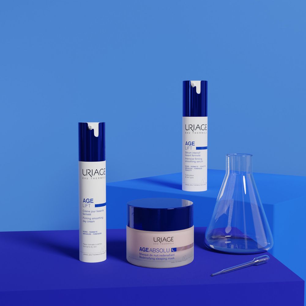 Tre prodotti Uriage su sfondo blu. Crema giorno, siero, maschera notte. Accessori da laboratorio.