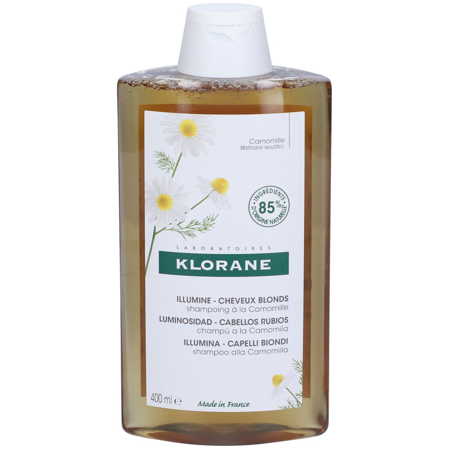 Flacone di shampoo Klorane. Liquido giallo, tappo bianco. Etichetta con fiori di camomilla, 85% ingredienti naturali. Per capelli biondi.