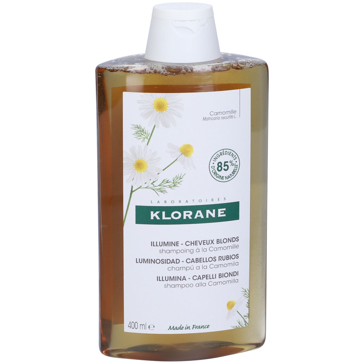 Flacone di shampoo Klorane. Liquido giallo, tappo bianco. Etichetta con fiori di camomilla, 85% ingredienti naturali. Per capelli biondi.