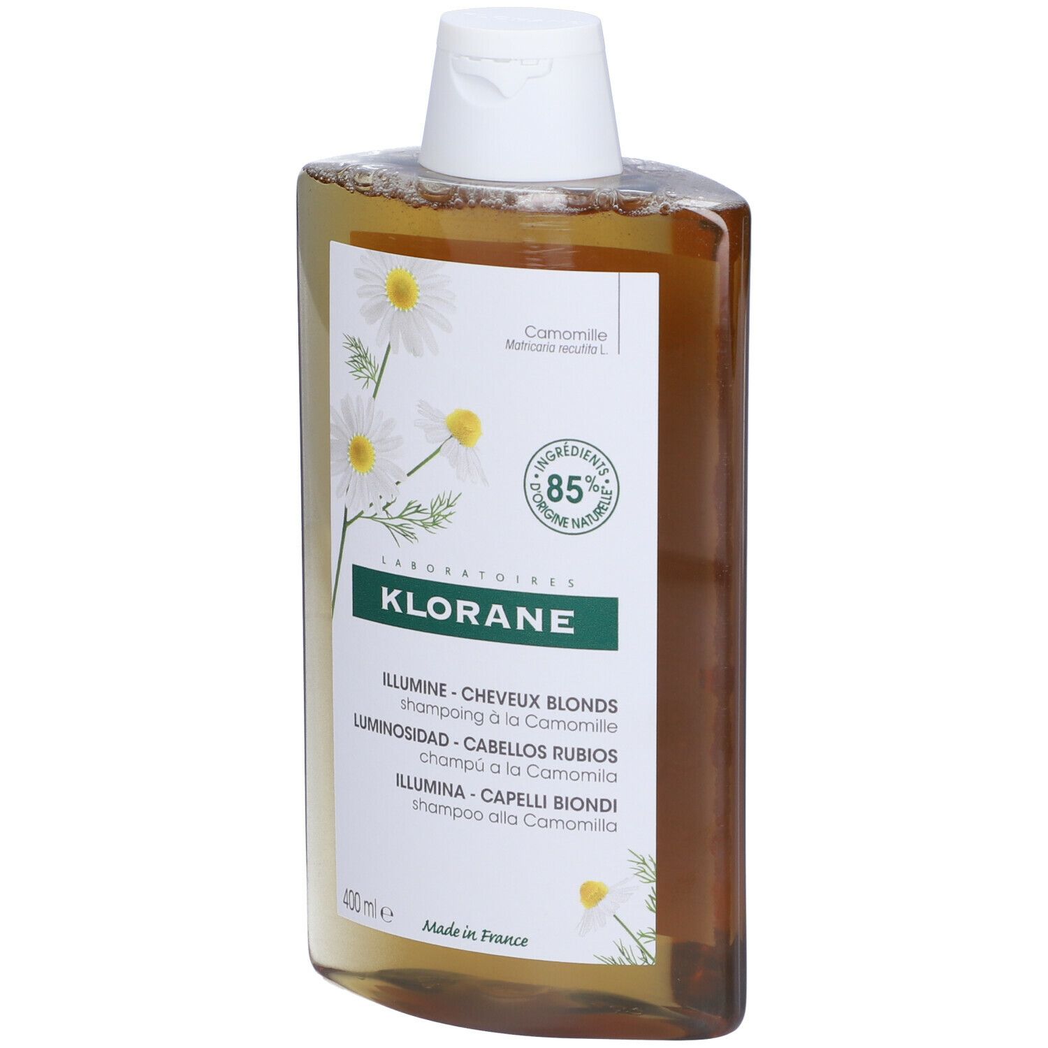 Flacone di shampoo Klorane. Liquido giallo, tappo bianco. Etichetta con fiori di camomilla, 85% ingredienti naturali. Per capelli biondi.