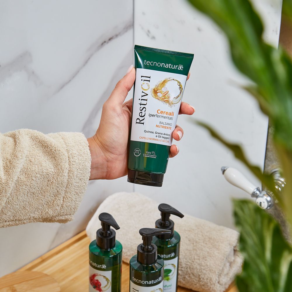 Mano che tiene un tubo verde. Altri prodotti sullo sfondo. Contesto bagno. Prodotto per capelli normali e secchi.
