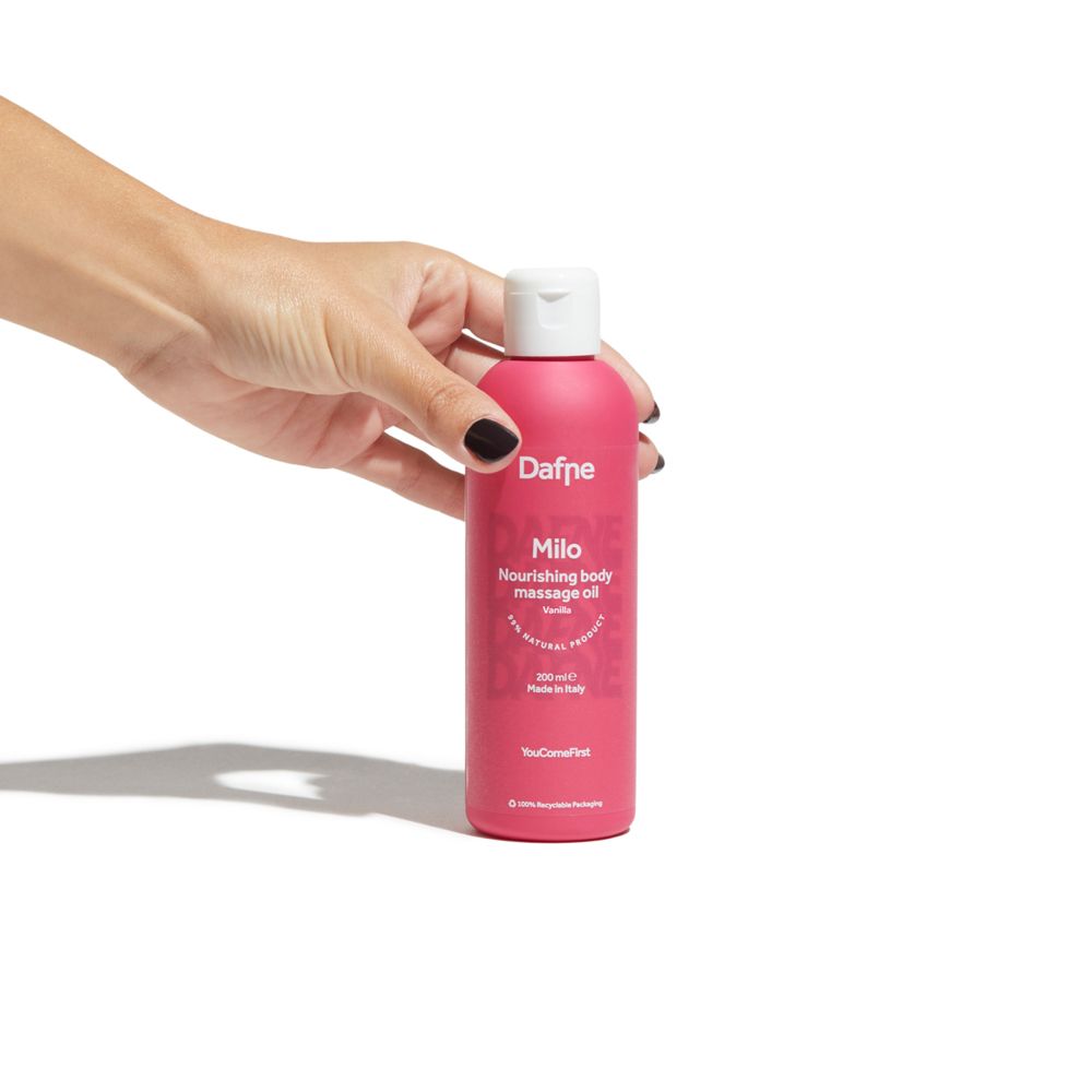 Mano che tiene flacone rosa con tappo bianco. Scritta: Dafne Milo, olio massaggio corpo Vaniglia.