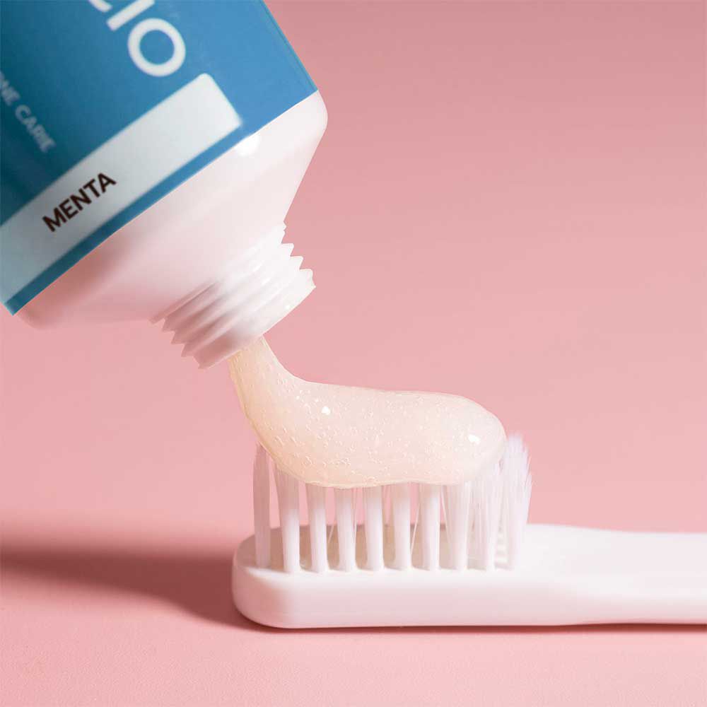 Zahncreme wird auf eine Zahnbürste gedrückt. Rosa Hintergrund. Tube mit Aufdruck.