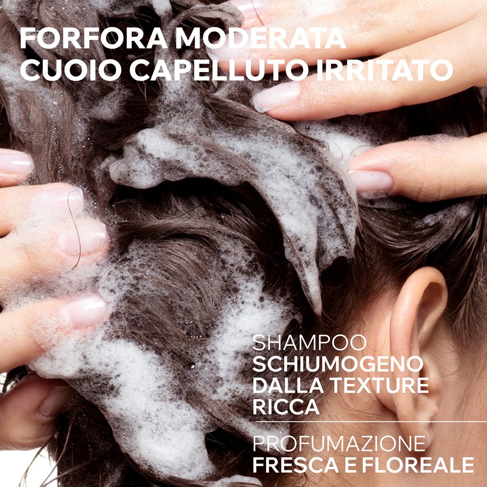 Hände massieren schäumendes Shampoo in dunkles Haar. Text auf Italienisch: "Mäßige Schuppen, gereizte Kopfhaut".