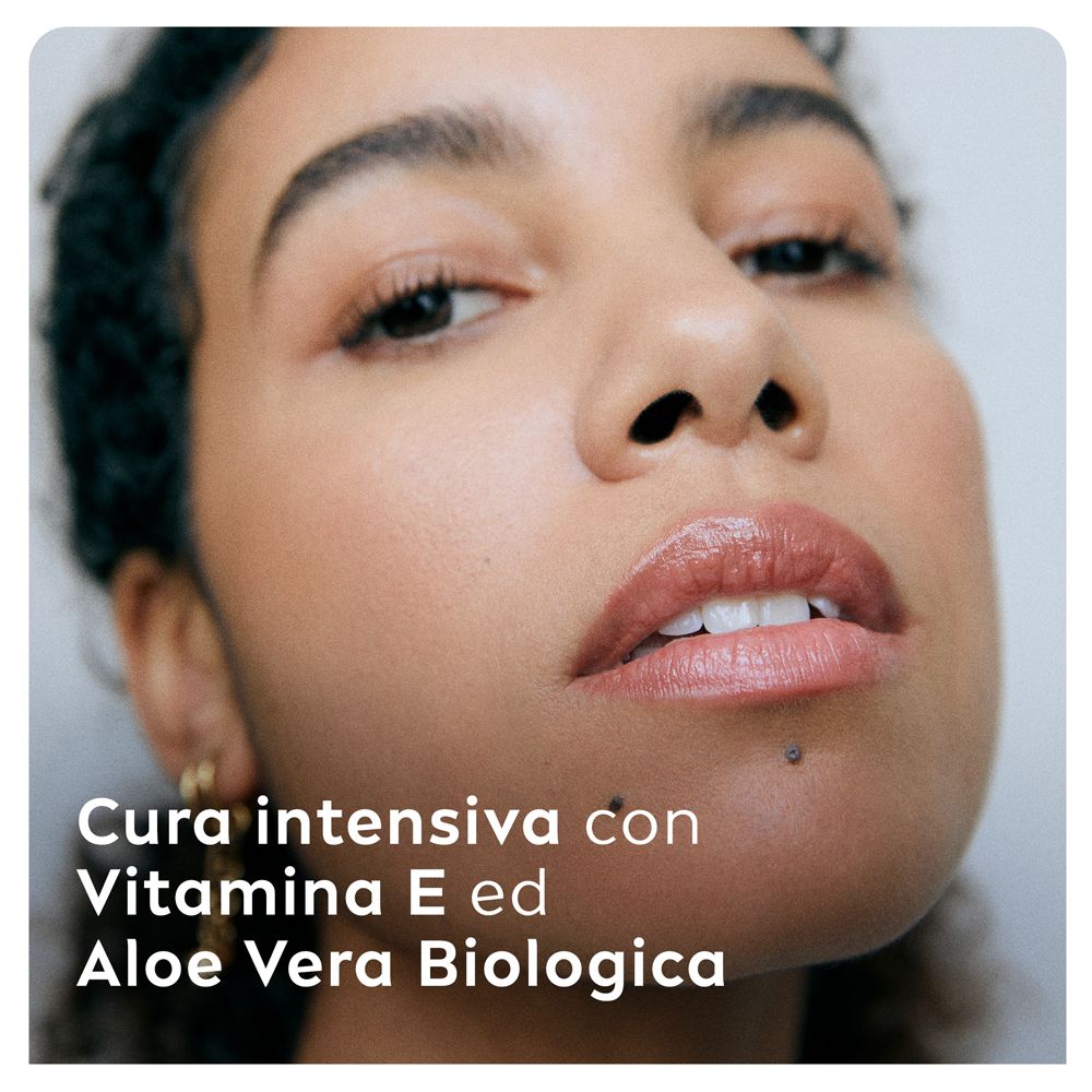 Primo piano di una donna. Testo: Cura intensiva con Vitamina E e Aloe Vera Biologica. Pelle e labbra.