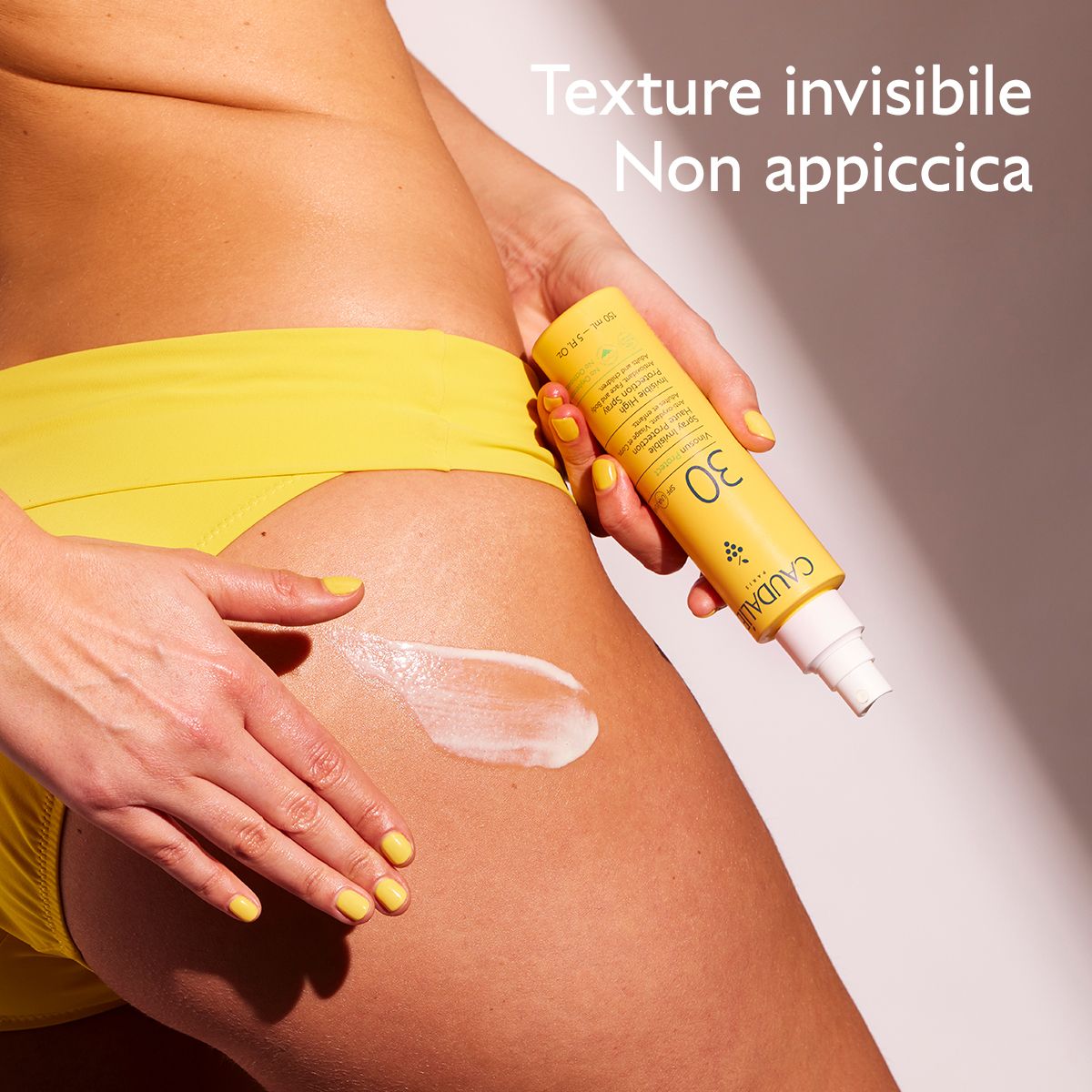 Persona che spruzza la protezione solare sulla pelle. Flacone giallo con vaporizzatore. Caudalie Vinousun Protect 30.