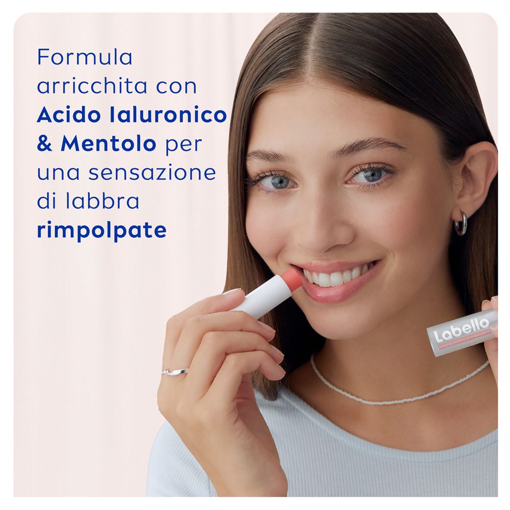 Giovane donna con balsamo labbra Labello. Applicazione sulle labbra. Rossetto rosa. Prodotto bianco.