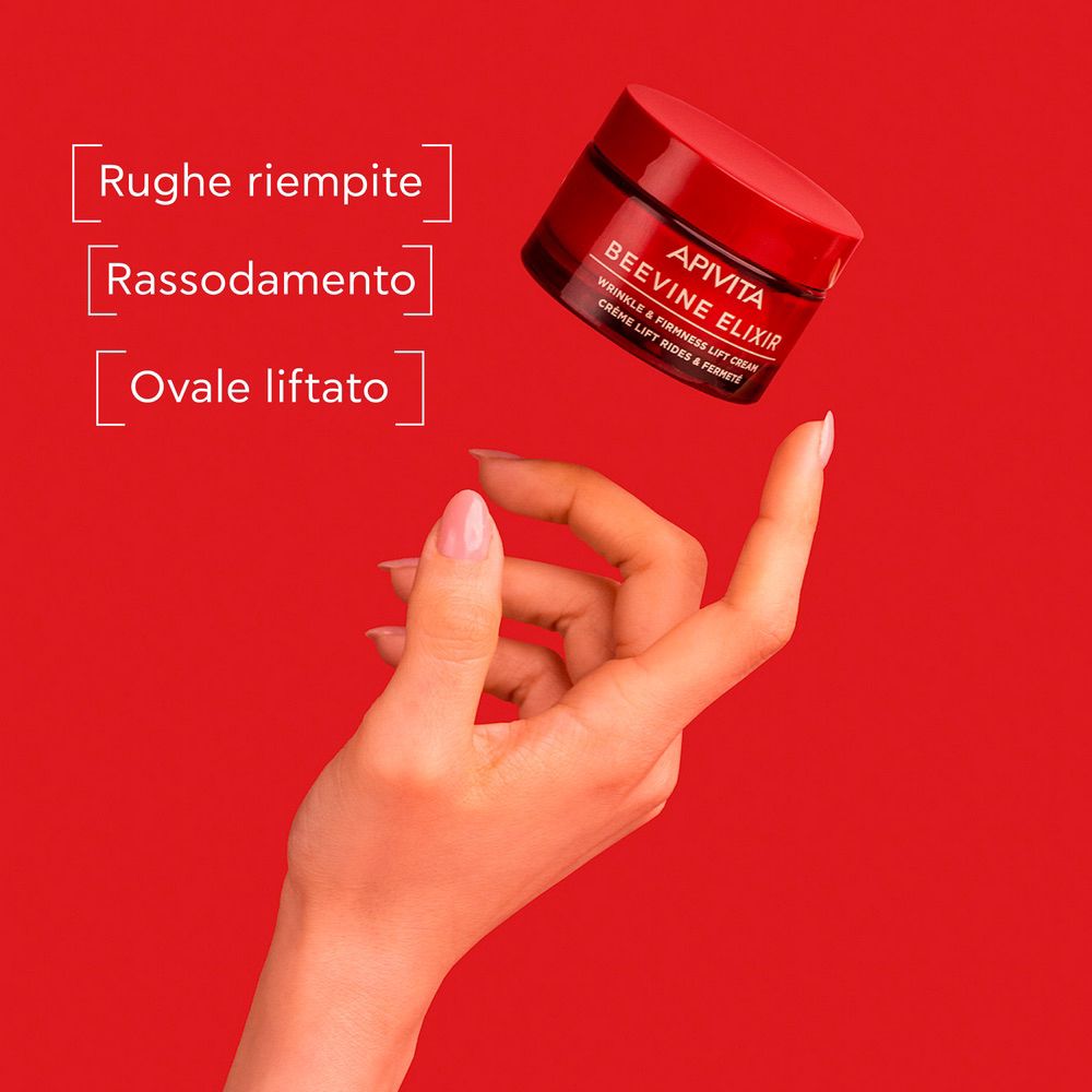 Vaso di crema rosso in aria, tenuto da una mano. Testo: APIVITA BEEVINE ELIXIR. Testo: WRINKLE & FIRMNESS LIFT CREAM. Crème lift rides & fermeté.