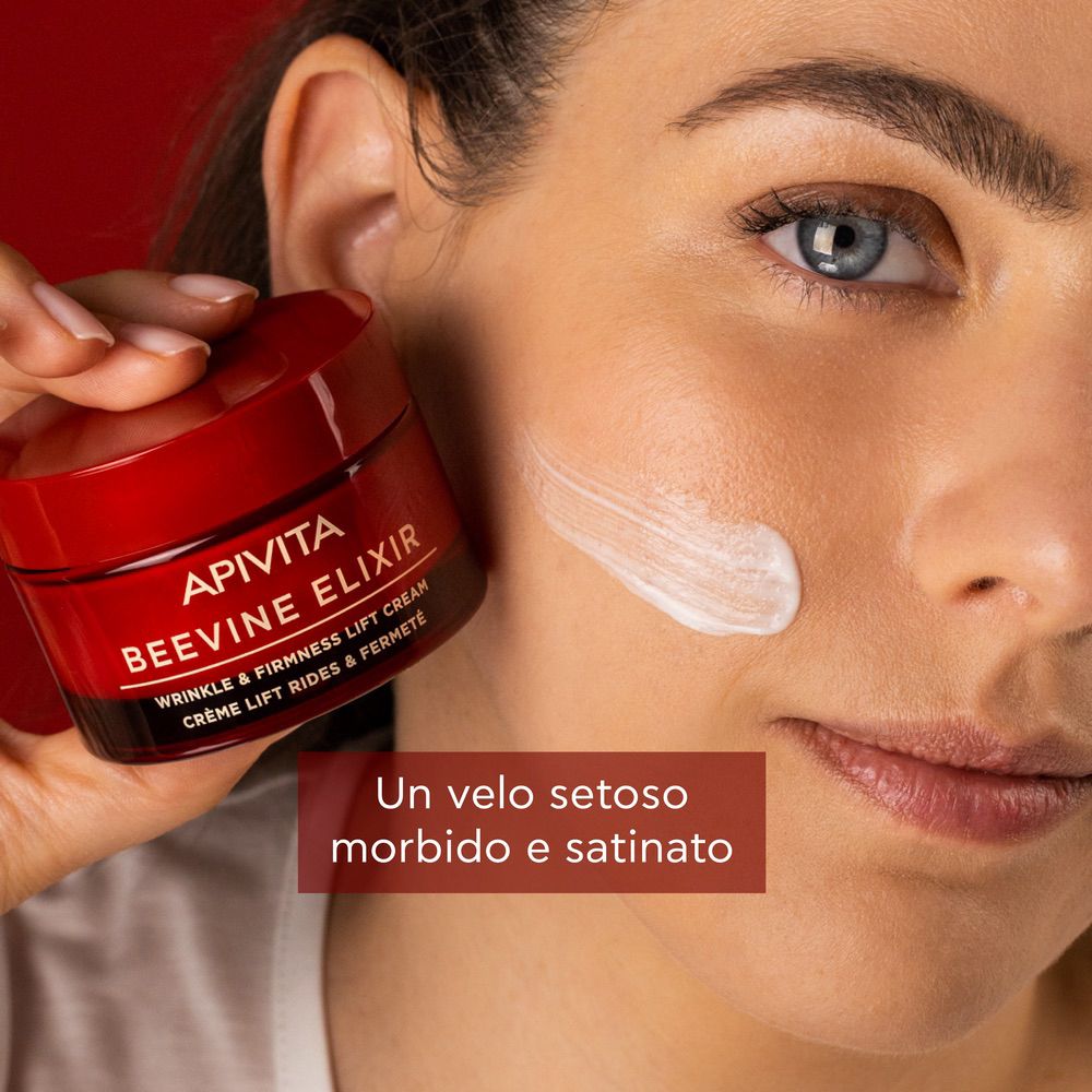 Donna con crema sul viso. Testo: APIVITA BEEVINE ELIXIR. Testo: WRINKLE & FIRMNESS LIFT CREAM. Crème lift rides & fermeté. Un velo setoso morbido e satinato.