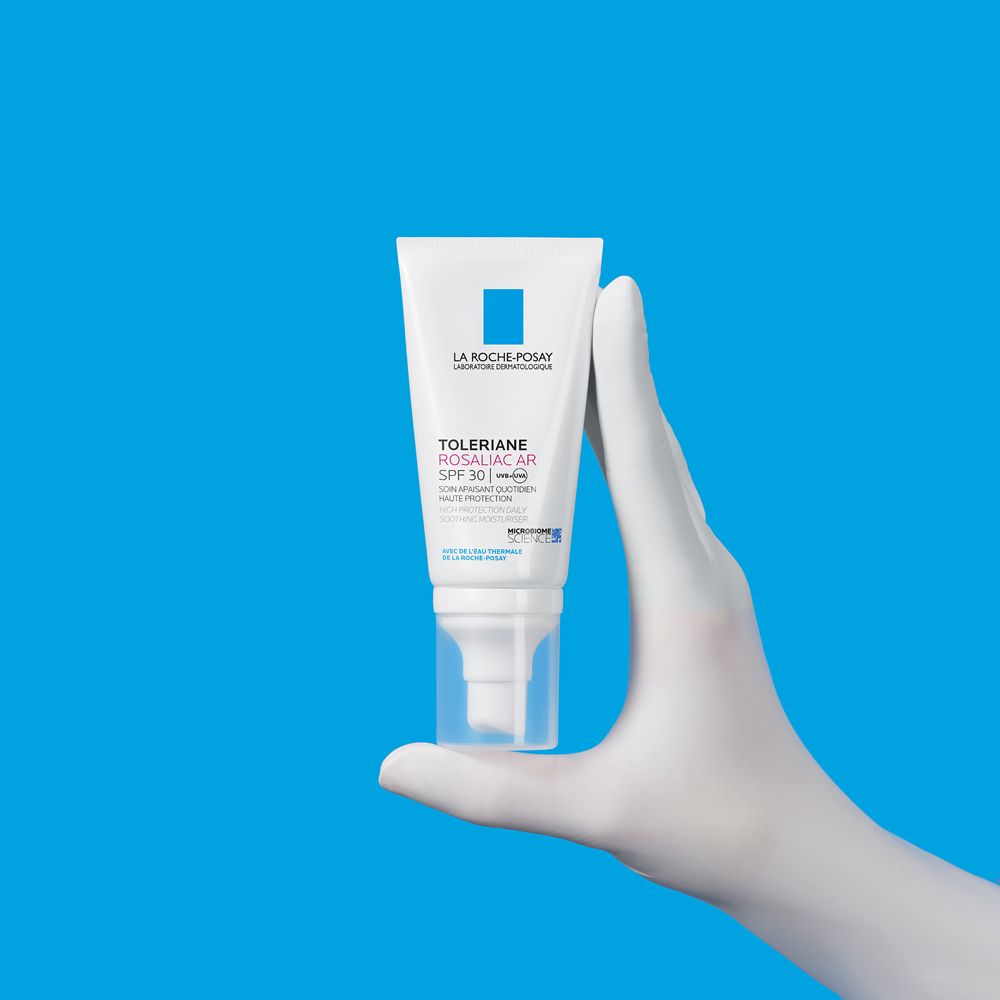La Roche-Posay Toleriane Rosaliac AR SPF 30. Tubo in mano. Sfondo blu.
